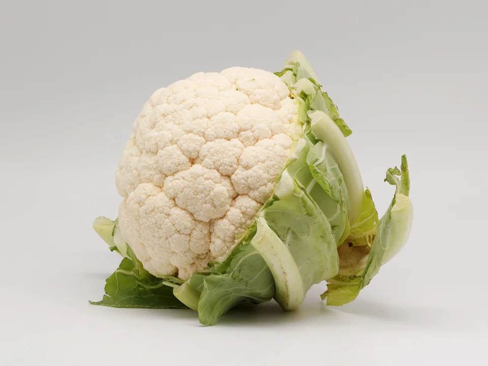 A white cauliflower head surrounded by green leaves